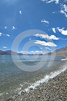 A view on the lake Pangong Tso with Himalaya mountain ranges surrounding its water and blue skies.