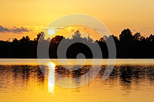 View of the lake at sunset, trees and sun reflection in the water