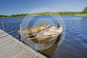 View of lake with two boats parked in shore on blue sky background.