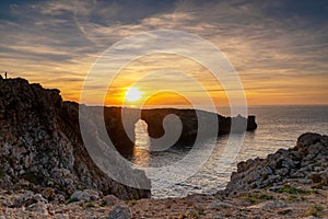 view of the landmark stone arch of Pont d\'en Gil on Menorca Island at sunset