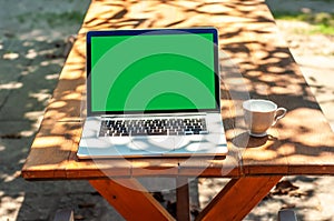 View on a laptop pc with a green screen and a coffee mug on a table in the garden