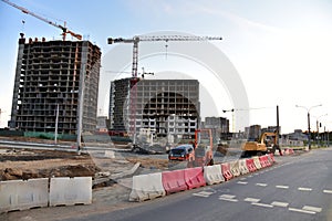 View on the large construction site with tower cranes and buildings on sunset background.  Road work and excavation for laying