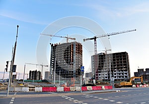 View on the large construction site with tower cranes and buildings on sunset background.  Road work and excavation for laying