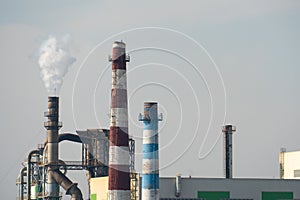 A view of a large factory or enterprise with large smoking chimneys against a blue sky. Environmental pollution by industrial