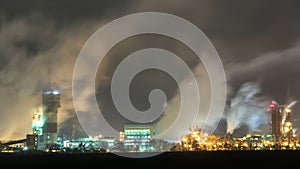 View of a large factory or plant in the light of night lighting. A lot of smoke comes out of the factory\'s chimneys.