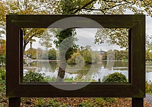 View through large hollow picture frame of trees and pond