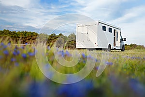 View of a large mobile home (design of van was changed during post processing ) parked in blooming meadow