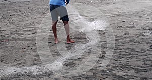 View of the legs of a fisherman on beach who collects fishing net and repairs it