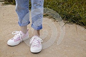 A view of the legs of a teenage girl in pink sneakers and blue jeans against a background of yellow dry grass. The