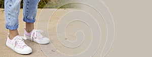 A view of the legs of a teenage girl in pink sneakers and blue jeans against a background of yellow dry grass. The