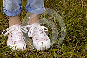 A view of the legs of a teenage girl in pink sneakers and blue jeans against a background of yellow dry grass. The