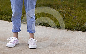 A view of the legs of a teenage girl in pink sneakers and blue jeans against a background of yellow dry grass. The