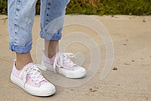 A view of the legs of a teenage girl in pink sneakers and blue jeans against a background of yellow dry grass. The