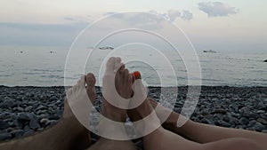 View on the legs of a young guy and a girl lying on the shore of the blue sea. Loving young couple lies on the seashore