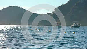 View of Liapades bay in Greece, focus on rather calm sea with small waves in foreground, blurred boats moving slowly with rocky