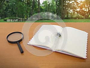 View of light bulb notebook and Magnifying glass on wooden table with green tree background