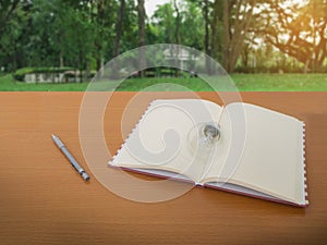 View of light bulb notebook and pencil on wooden table with green tree background