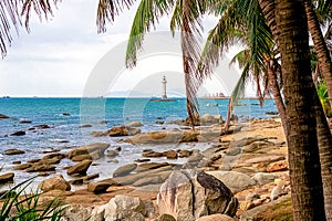 View of a lighthouse in the sea near a rocky shore with palm trees. Heavenly Grottoes Park, Sanya.