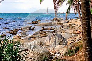 View of a lighthouse in the sea near a rocky shore with palm trees. Heavenly Grottoes Park, Sanya.