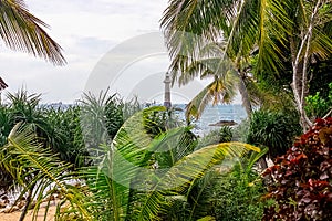 View of the lighthouse in the sea near the rocky shore through the palm trees. Sanya, China