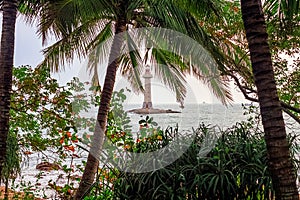 View of the lighthouse in the sea near the rocky shore through the palm trees. Sanya, China