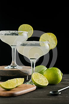 View of limes, lemons and two glasses of margarita cocktail, selective focus, black background,