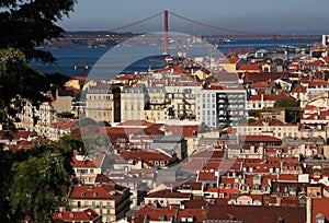 View of Lisbon\'s historic center with red-roofed houses and Ponte 25 de Abril across the Tajo River