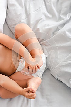 View of little baby in diaper laying on back and grabbing feet with hands