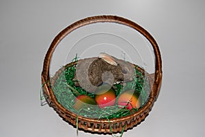 View on a little porcelain easter bunny and colorful easter eggs on a green grass in a basket with copy space