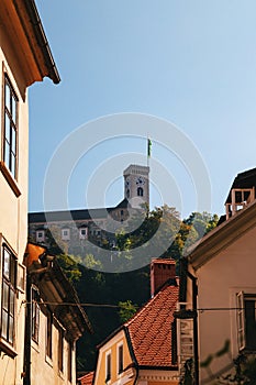 A view at Ljubljana Castle tower from a beautiful quiet narrow street with orange tiled roofs without people in the old