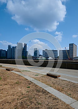 View of london tall buildings with parched grass park under blue sky with puffy clouds