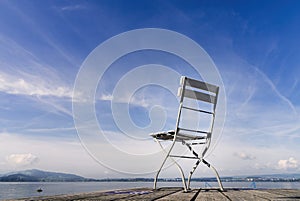 View of a lonely and empty chair with a landscape of a calm lake with blue sky and light clouds. With copy space in the upper left