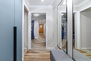 View of the long corridor in the modern apartment from the hallway with large mirrors and wardrobe