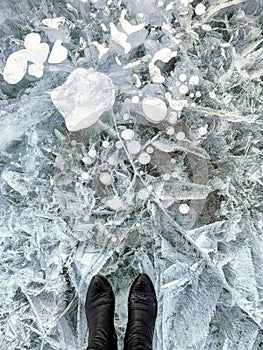 A view looking down at a pair of feet standing on frozen ice of a lake with interesting bubbles and patterns.