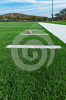 View looking down the sideline of an American football field with line markers and football.
