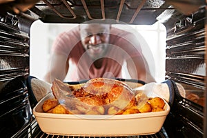 View Looking Out From Inside Oven As Man Cooks Sunday Roast Chicken Dinner