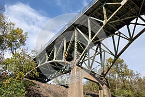 View looking up at an old bridge showing structural deficiencies, rusted metal and crumbling concrete details photo