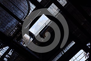 View looking up and out from a dark industrial space through grids and furnaces to blue sky beyond