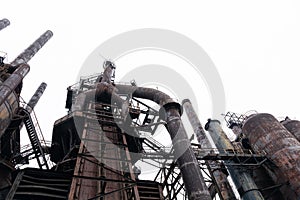 View looking up of rusting derelict steel mill structures against a gray sky in winter