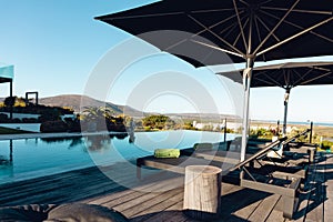 View of luxury contemporary outdoor wooden patio with swimming pool with deck chairs and umbrellas