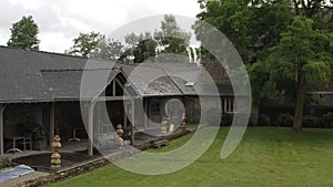 View of luxury grey stone house and terrace near the garden and large old tree in summer day against cloudy sky. Action