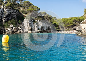 View of Macarelleta cove in the south of the island of Menorca, seen from the water with unrecognizable people sunbathing and a photo