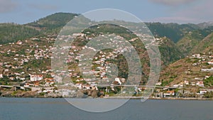 View of Madeira island with its cliffy shore, white houses and buildings, roads and trestles. View from sailing yacht