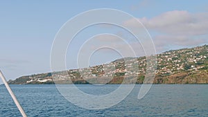 View of Madeira island with its cliffy shore, white houses and buildings, roads and trestles. View from sailing yacht