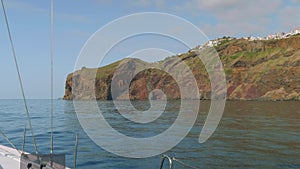 View of Madeira island with its cliffy shore, white houses and buildings, roads and trestles. View from sailing yacht