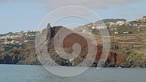 View of Madeira island with its cliffy shore, white houses and buildings, roads and trestles. View from sailing yacht