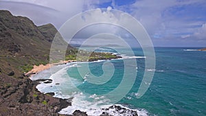 View of Makapuu beach. Waves of Pacific Ocean wash over yellow sand of tropical beach. Magnificent mountains of Hawaiian