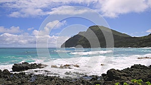 View of makapuu lighthouse. Waves of Pacific Ocean wash over yellow sand of tropical beach. Magnificent mountains of