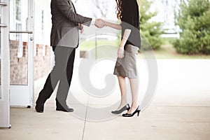 View of a male and a female wearing formal clothes while shaking hands, standing next to a building