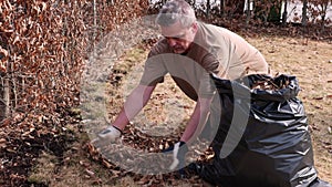 View of a man collecting fallen leaves in a plastic bag in a garden on a spring day.